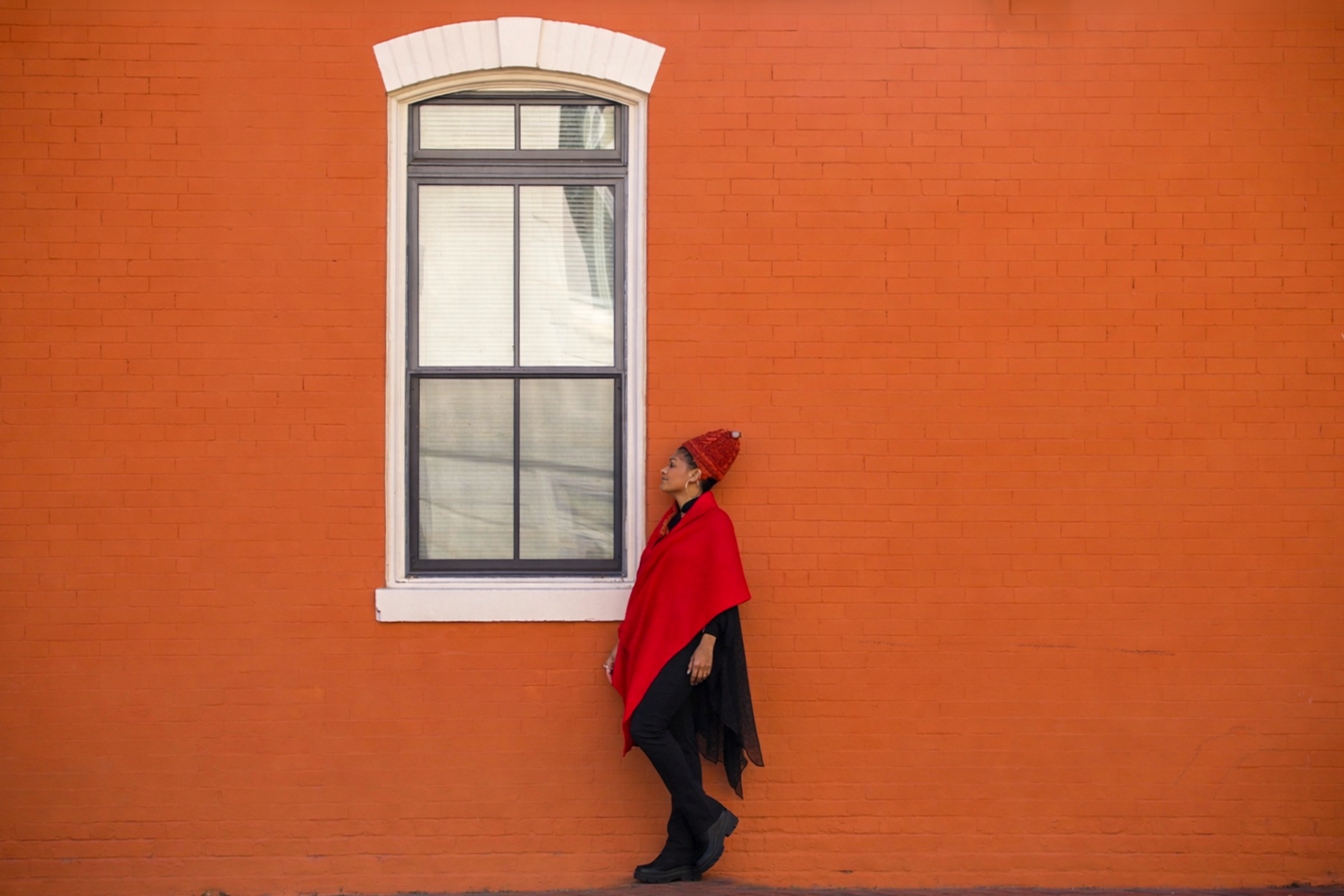 Traciana leaning against an orange brick wall